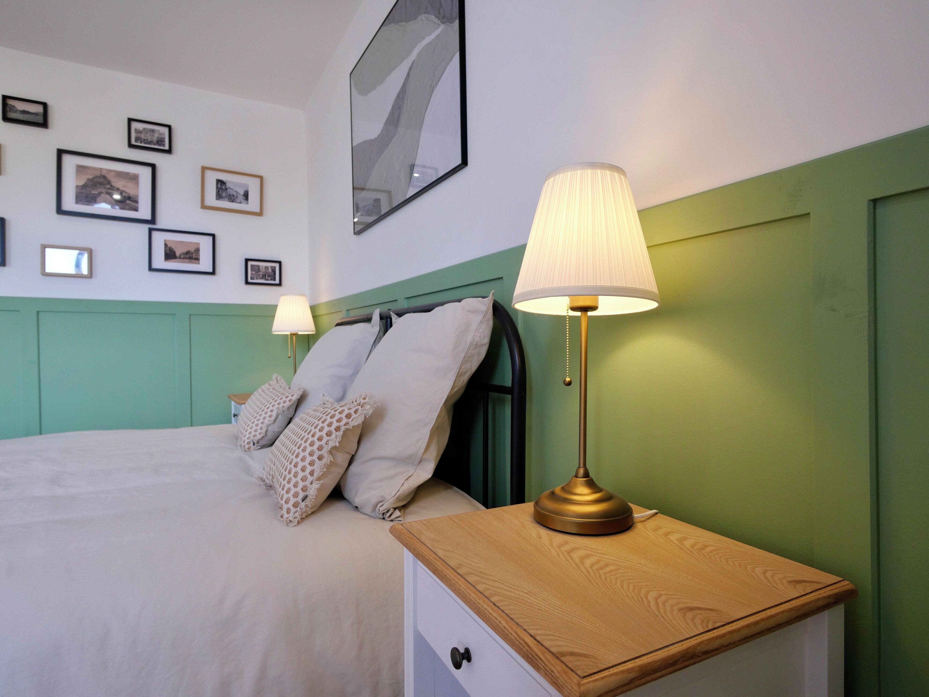 Une chambre à coucher bien rangée, avec un lit, des lampes de chevet et des tableaux encadrés accrochés au mur.