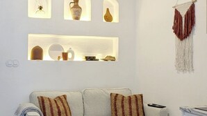 Een moderne woonkamer met een grijze bank, decoratieve kussens, een klein wit bijzettafeltje en wandplanken met vazen.