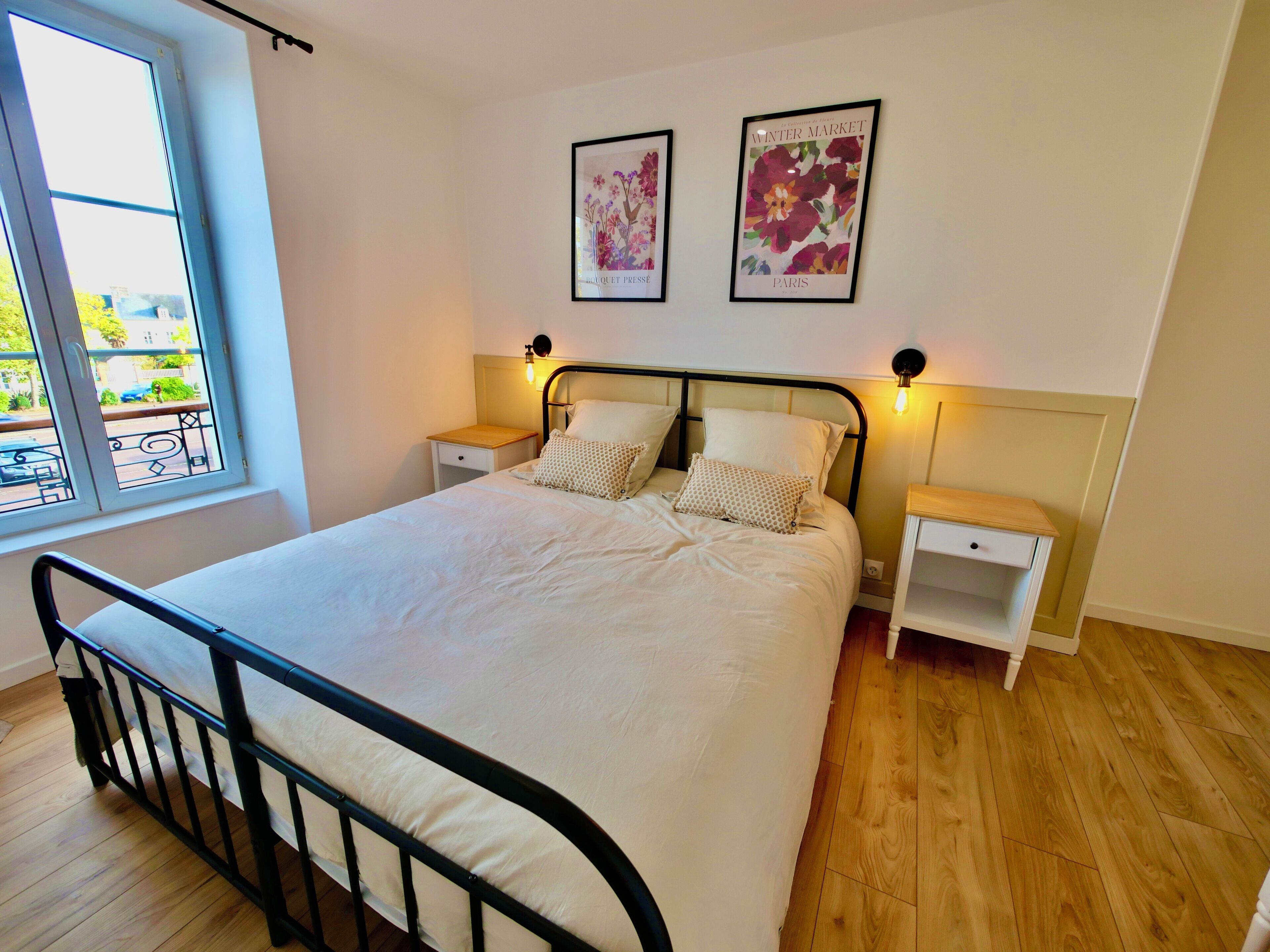 A bedroom with a bed, two nightstands, a window, and two wall-mounted pictures.