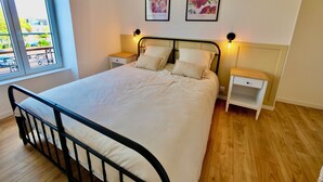 Un dormitorio con una cama, dos mesitas de noche, una ventana y dos cuadros colgados en la pared.