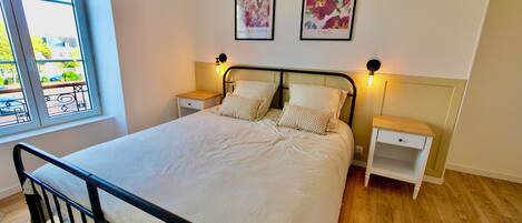 A bedroom with a bed, two nightstands, a window, and two wall-mounted pictures.