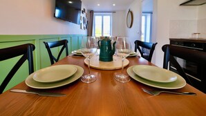 Una mesa de comedor dispuesta con platos, copas de vino y una jarrón, rodeada de sillas.