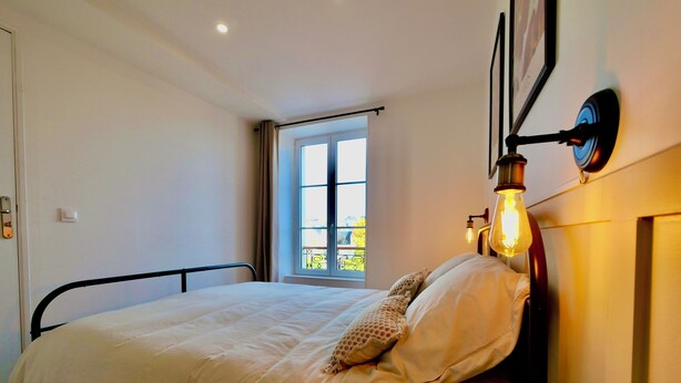 Un dormitorio con cama, ventana y lámpara de pared.