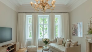 A spacious living room with a large chandelier, a sofa set, a coffee table, and a television. - Roosevelt Stadthaus (Vienna)