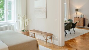 A spacious bedroom with a large bed, a wooden bench, and a dining area with chairs and a table. - Roosevelt Stadthaus (Vienna)