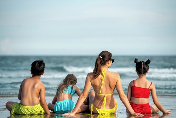 Vier Personen sitzen am Strand und blicken auf das Meer.