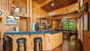 A wooden cabin interior with a kitchen, dining area, and bar with stools.