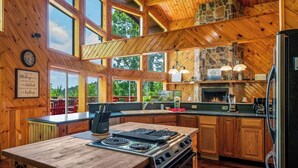 A spacious kitchen with wooden cabinets, a large island with a stove, and a stone fireplace.
