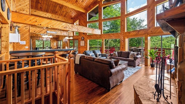 A spacious wooden interior with a dining area, seating, and large windows offering views of the outdoors.