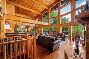 A spacious wooden interior with a dining area, seating, and large windows offering views of the outdoors. - Stunning views! Huge game room, vaulted ceilings, big bedrooms, & great parking! (Sevierville)