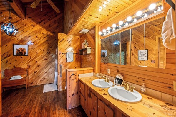 A wooden cabin bathroom with two sinks, a large mirror, and a wooden bench. - Stunning views! Huge game room, vaulted ceilings, big bedrooms, & great parking! (Sevierville)
