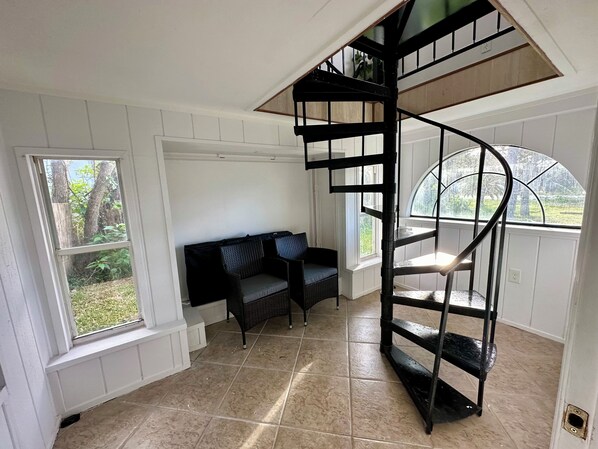 A room with a spiral staircase, a black sofa, and large windows. - Charming St Augustine Cottage, 6 minute walk to the beach, on Anastasia Island (St. Augustine)