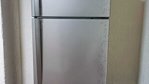 A stainless steel refrigerator with a two-door design, located in a corner of a room with wooden flooring and white walls. - Princesa Department. Huatulco. (Santa Cruz Huatulco.)