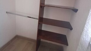 A corner of a room with a wooden shelf unit against the wall and a metal rod. - Princesa Department. Huatulco. (Santa Cruz Huatulco.)