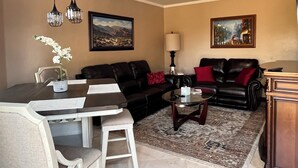 A living room with a dining area, a black leather sofa, a coffee table, and a painting on the wall. -  1 bedroom guest house in quiet, gated community. (Poway)