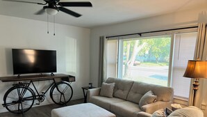 Un salon comprenant un canapé, un pouf et un téléviseur posé sur un meuble en bois.