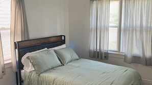 Une chambre à coucher avec un lit, un plancher en bois, un ventilateur de plafond et des fenêtres avec des rideaux.