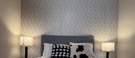 A neatly made bed with white linens and two black and white patterned pillows, flanked by two bedside lamps on either side.