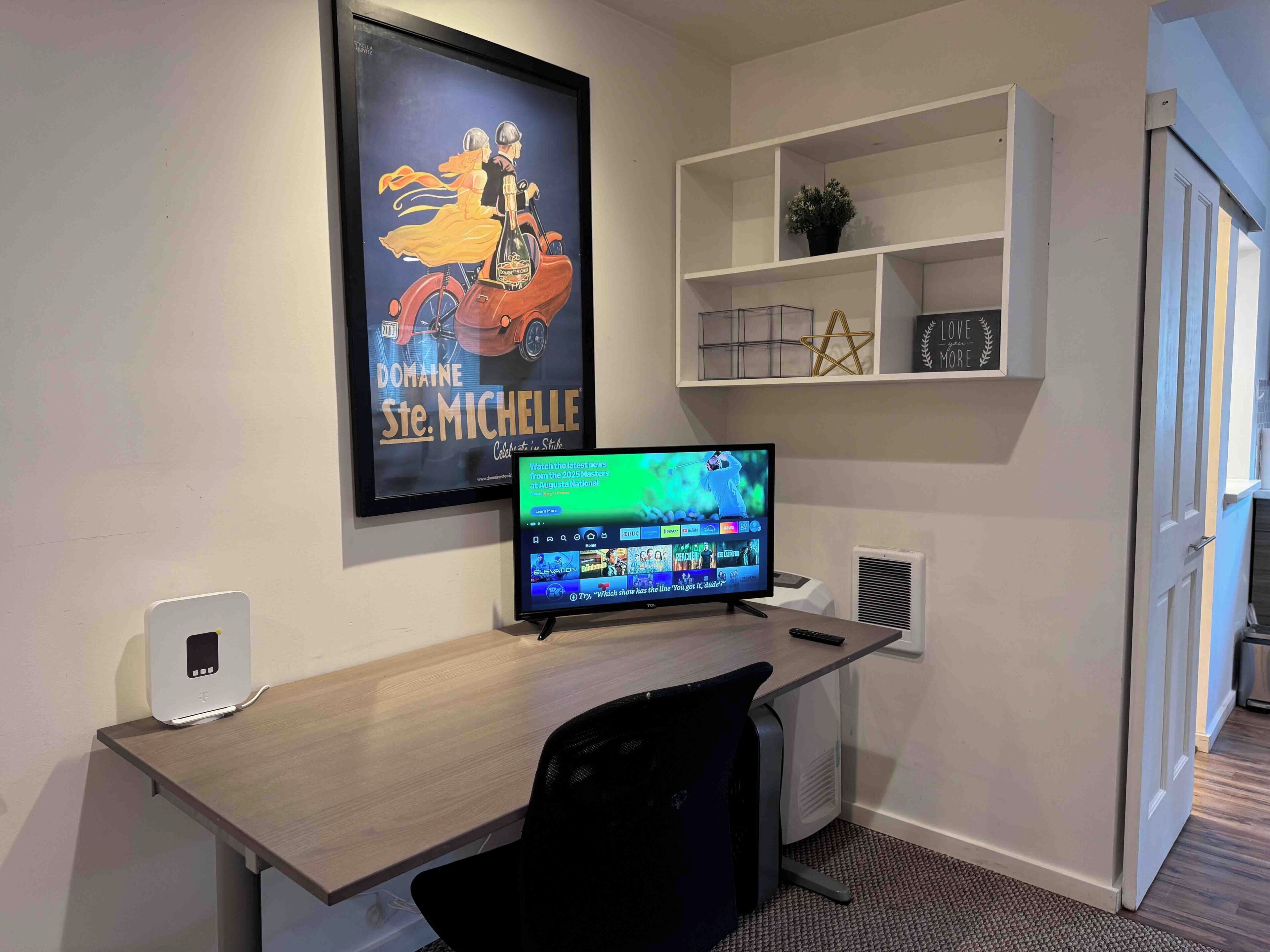 Um espaço de escritório moderno com uma mesa, cadeira, monitor de computador e um pôster emoldurado na parede.