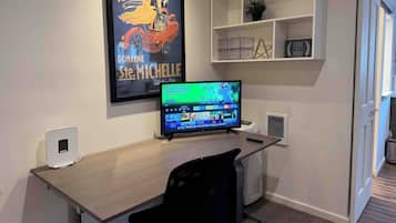 Um espaço de escritório moderno com uma mesa, cadeira, monitor de computador e um pôster emoldurado na parede.