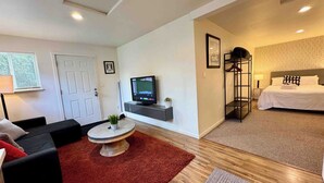 Une chambre d’hôtel moderne équipée d’une télévision, d’un lit, d’un coin salon avec un tapis rouge et d’une petite table agrémentée d’une plante.
