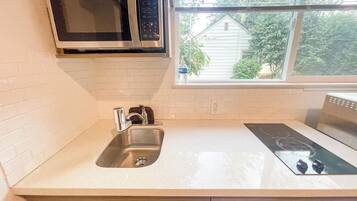 A kitchen with a stainless steel sink, a microwave, and an induction cooktop.