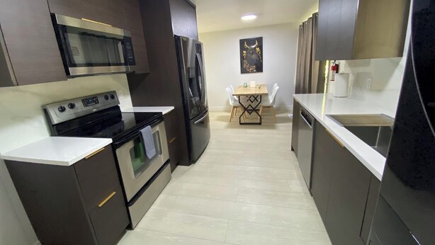 Una cocina moderna con armarios oscuros, electrodomésticos de acero inoxidable y piso de color claro.