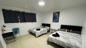 Una habitación con dos camas individuales, un escritorio, una silla y un ventanal con cortinas.