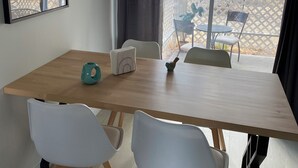 Un comedor con una mesa de madera, sillas blancas y vistas a un patio exterior con valla y sillas blancas.