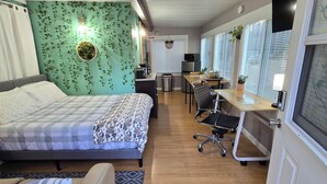 A bedroom with a bed, bedside tables, a desk with a chair, a small kitchenette, and a bathroom with a toilet and sink.