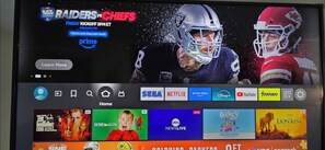 Televisioruudulla näkyy urheilutapahtuma, jossa pelaavat Raiders ja Chiefs. Ruudussa on myös Prime Videon logo ja painike, jossa lukee ”Lue lisää”.