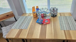 A wooden dining table with two cushioned chairs, a bottle of Delight, a bottle of French Vanilla, a bottle of Water, a can of Coca-Cola, a pack of Munchos, and a pack of Nutella.