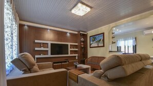 A modern living room with a flat-screen TV, wooden shelving, a wicker chair, and a sofa. - Stillo Gramado Dutra (Gramado)
