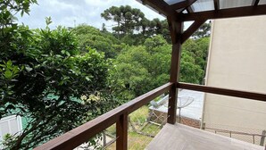 A wooden deck with a glass roof overlooking a lush garden and a body of water. - Stillo Gramado Dutra (Gramado)