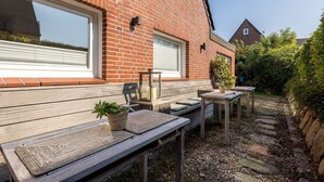 Un área de patio con bancos y mesas de madera, una planta en maceta y un farol.