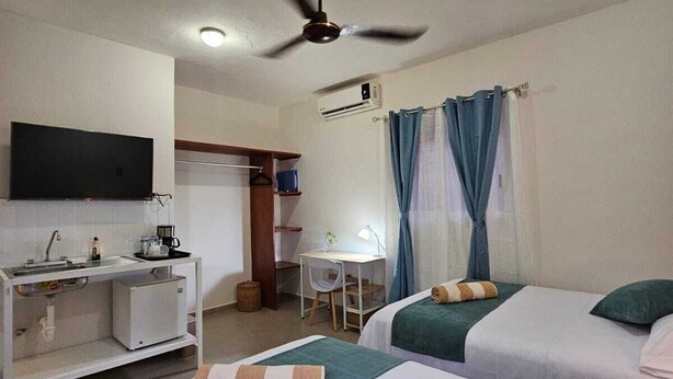 Une chambre d’hôtel avec deux lits, un bureau, une chaise, une télévision et un ventilateur de plafond.