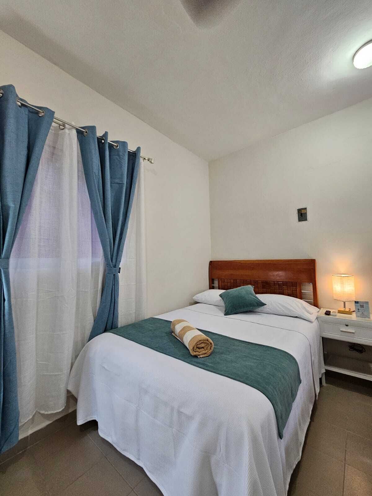 A neatly made bed with a green and white bedspread, a rolled towel, and a wooden headboard.