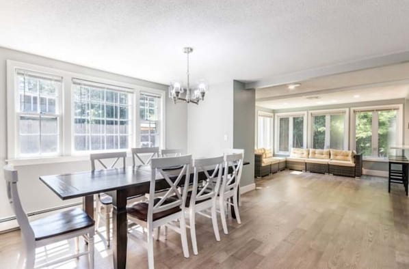 A spacious dining area with a long table and chairs, large windows, and a built-in bench along the wall.