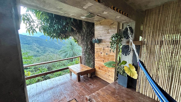 A wooden deck with a bench, a doormat, and a view of a lush landscape.