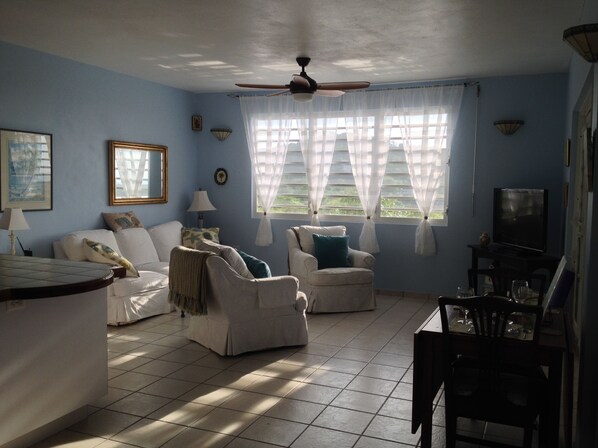 Una sala de estar con ventilador de techo, televisor y comedor con sillas y una mesa.
