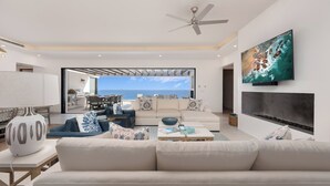 Ein modernes Wohnzimmer mit großem Fernseher, Deckenventilator und Meerblick.