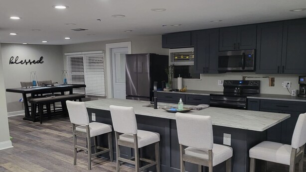 A modern kitchen with a central island, bar stools, and dark cabinetry. - Snow Bird Alert -3 Month Rental - Venice Isle Estates -2 Bed 2 Bath House  (Venice)