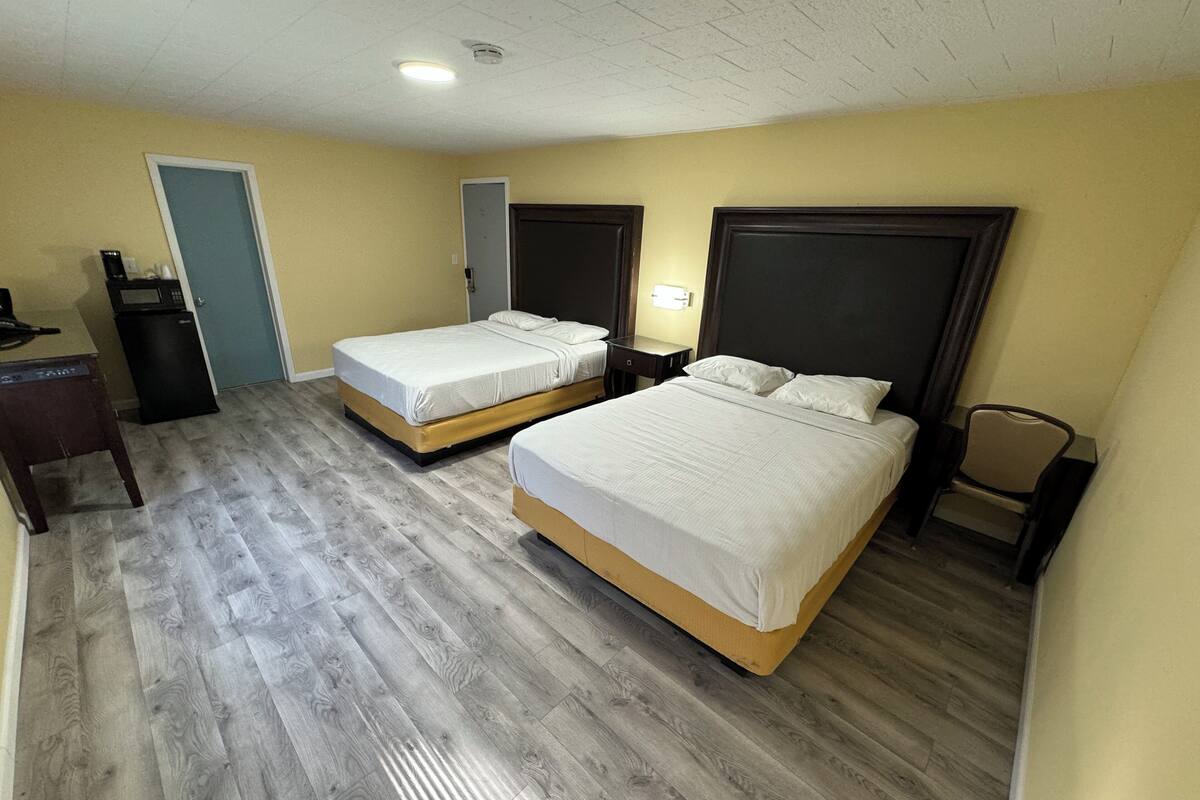 A hotel room with two beds, a desk, a chair, a microwave, and a door.