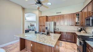 A kitchen with wooden cabinets, granite countertops, a stainless steel refrigerator, and a ceiling fan. - Cactus Bloom - Cozy Desert Retreat in Chandler (Chandler)