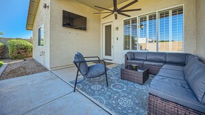 A covered patio area with a ceiling fan, a large window, and a seating area with a sofa and chairs. - Cactus Bloom - Cozy Desert Retreat in Chandler (Chandler)