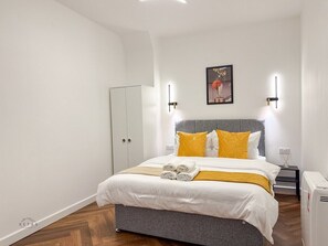A bedroom with a bed, a wardrobe, a bedside table, and a wall-mounted light fixture. - Modern 2 Bedroom Flat in Luton Town Centre (Luton)