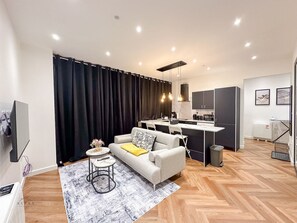A modern living room with a sofa, coffee table, and a kitchen area with a dining table. - Modern 2 Bedroom Flat in Luton Town Centre (Luton)