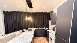 Eine kompakte Küche mit Marmorarbeitsplatte, einer Waschmaschine und einem Essbereich mit einer Couch.