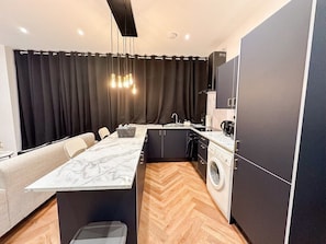 A compact kitchen with a marble countertop, a washing machine, and a dining area with a sofa. - Modern 2 Bedroom Flat in Luton Town Centre (Luton)