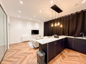 A modern kitchen with a marble countertop, black cabinets, and a black curtain. - Modern 2 Bedroom Flat in Luton Town Centre (Luton)